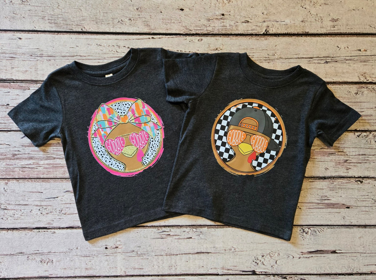 Two dark heather toddler short sleeve tees with girl and boy Gobble Gobble turkey designs